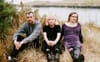 Sean Nolan, Constance Keane, and Jamie Hyland sitting in grass by water.