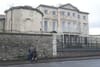 Aldborough House behind a wall as three people walk past. Photo by Sam Tranum.