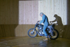 Stephen Skrynka on a motorcycle next to his wooden Wall of Death, casting a shadow on it.