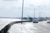 Seawater sprays over the a low wall, puddling on a big road as it runs along the coast in Sandymount.