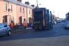 Two men in high-viz trail a waste collection truck as it trundles down a street past a two-storey redbrick terrace in Inchico