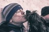 A man standing against a wall gets a kiss from a shaggy dog.
