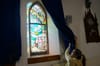 A woman is in the right side of the frame, and she is pulling back a curtain on a colourful stained-glass window and light st
