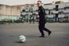 A boy kicks a ball in a grey concrete lot.
