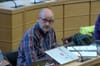 A man sits behind long table, with documents in front of him.