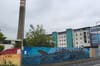 A colourful hoarding runs around a vacant site in Ballymun. Behind is a tall chimney.