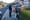 A man stands at the gate to a driveway to chat to a neighbour while a dog yaps and plays around.