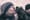 A man standing against a wall gets a kiss from a shaggy dog.