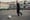 A boy kicks a ball in a grey concrete lot.