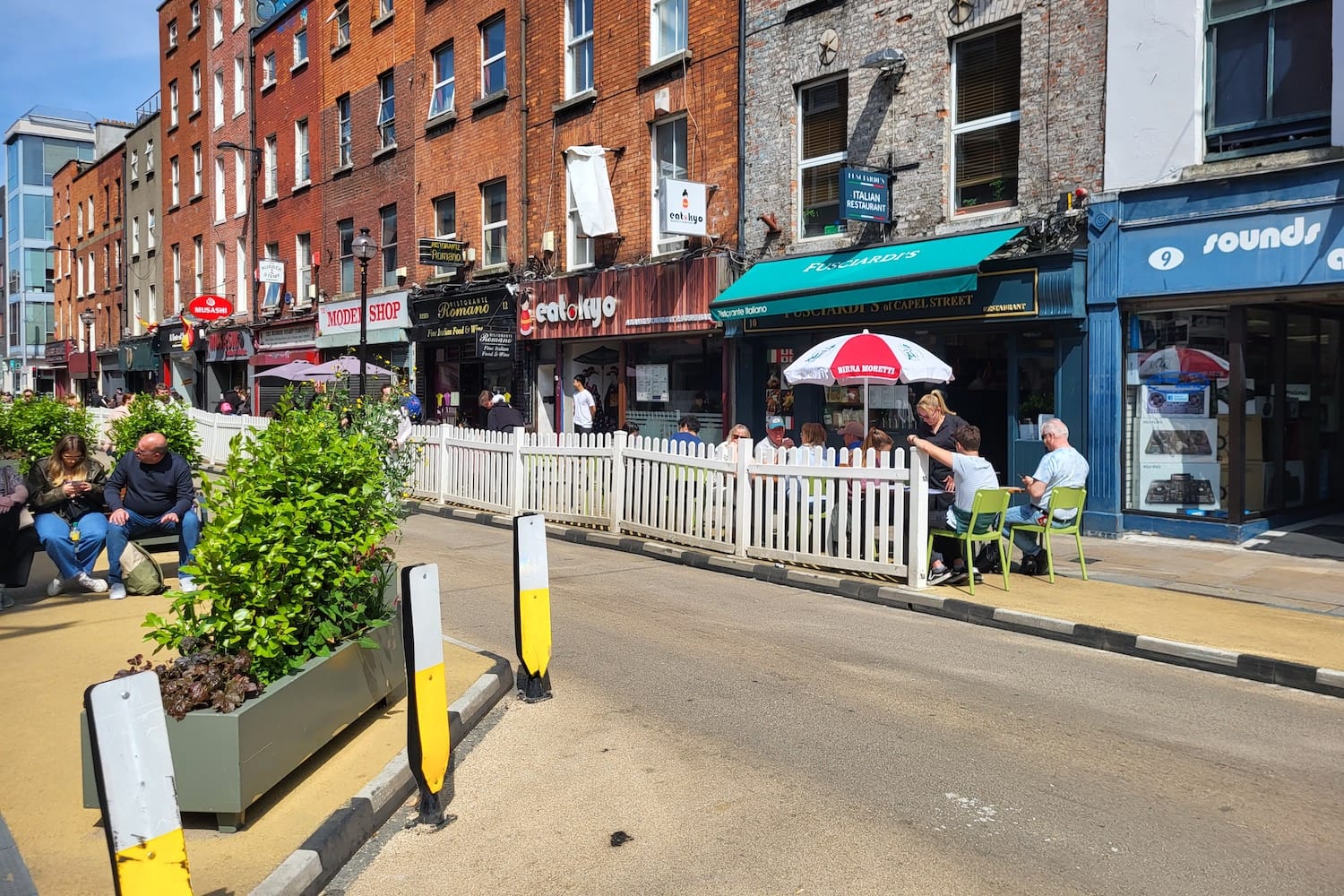 White picket fencing on a pedestrainised street, and an umbrella with branding on it.