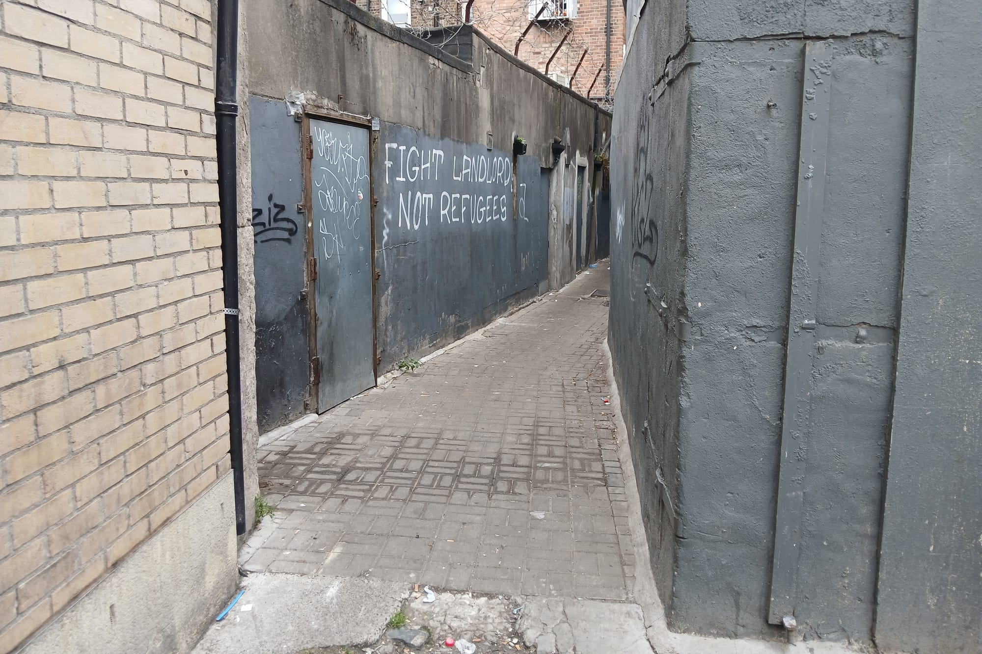 A paved laneway in Dublin that councillors want to close.  A path runs between two tall walls. On one wall, graffiti reads: "Fight landlords not refugees"