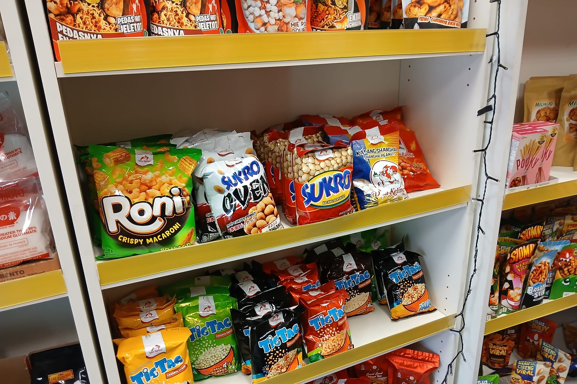 Three wooden shelves are stacked with colourful shiny packets of Indonesian snacks.